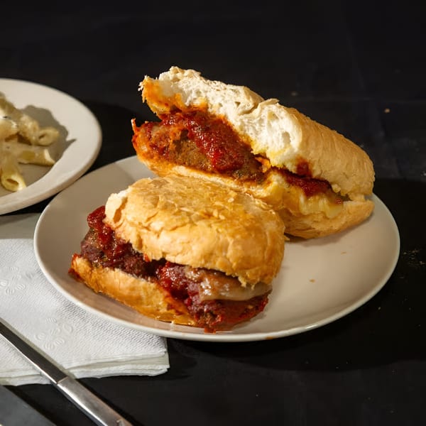 Two halves of a meatball sub sandwich with red sauce and cheese on a white plate.
