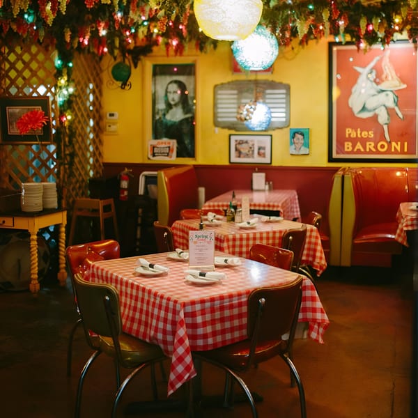 Cozy Italian restaurant interior with red and white checkered tablecloths, red booths, and festive string lights.