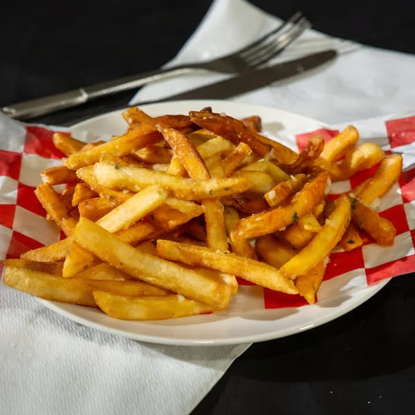 A plate of golden-brown french fries with seasoning, served on a white plate with red and white checkered paper.