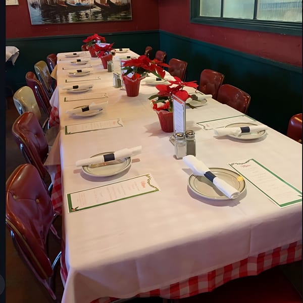 Long dining table set with white tablecloths, red checkered skirts, plates, and poinsettia centerpieces at Monjunis.