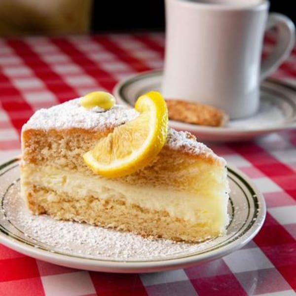 A slice of lemon cake with powdered sugar and a lemon wedge on a red and white checkered tablecloth.