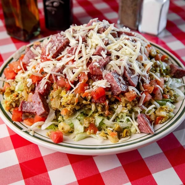 Monjunis Italian salad with shredded lettuce, diced tomatoes, salami, and shredded cheese on a red and white checkered tablecloth.