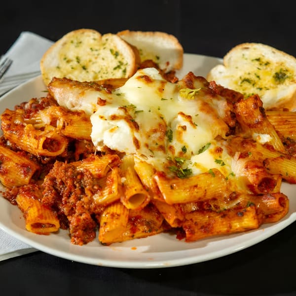 Baked ziti pasta with meat sauce, melted cheese, and garlic bread on a white plate.