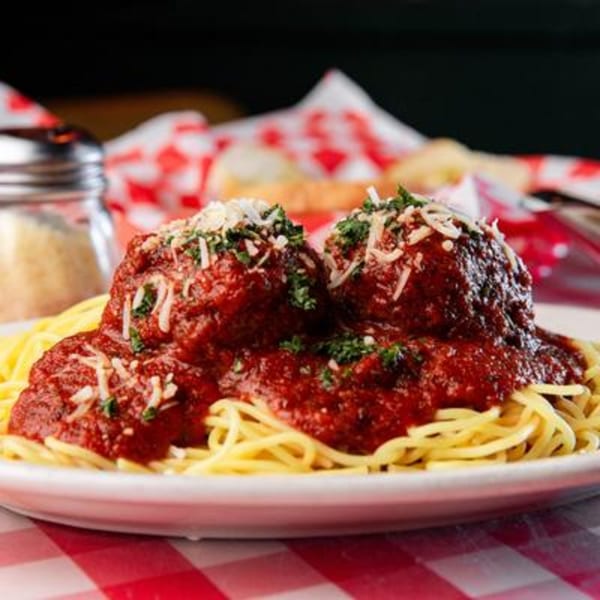 Spaghetti with two large meatballs, marinara sauce, grated cheese, and parsley on a white plate.